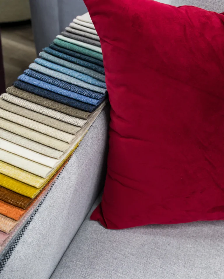 Fabric swatches next to a deep red pillow on a grey couch.